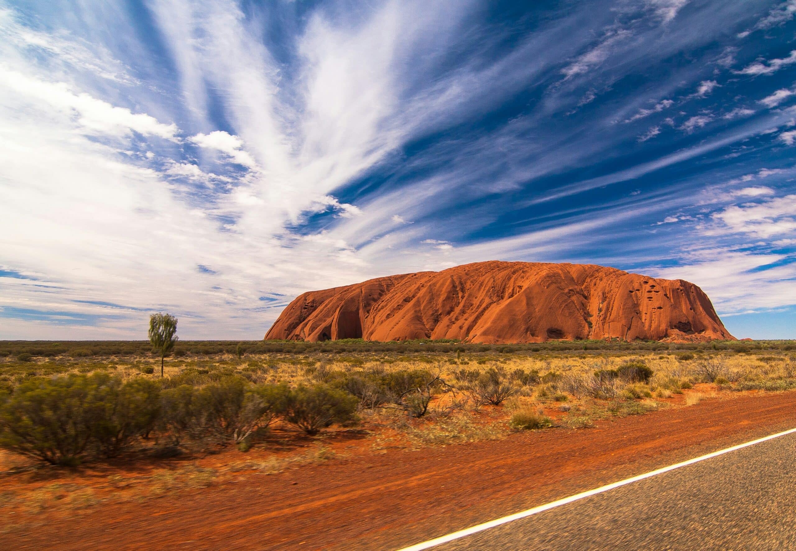 http://Vue%20d'Uluru,%20le%20célèbre%20monolithe%20du%20Territoire%20du%20Nord,%20sous%20un%20ciel%20aux%20nuages%20étirés.