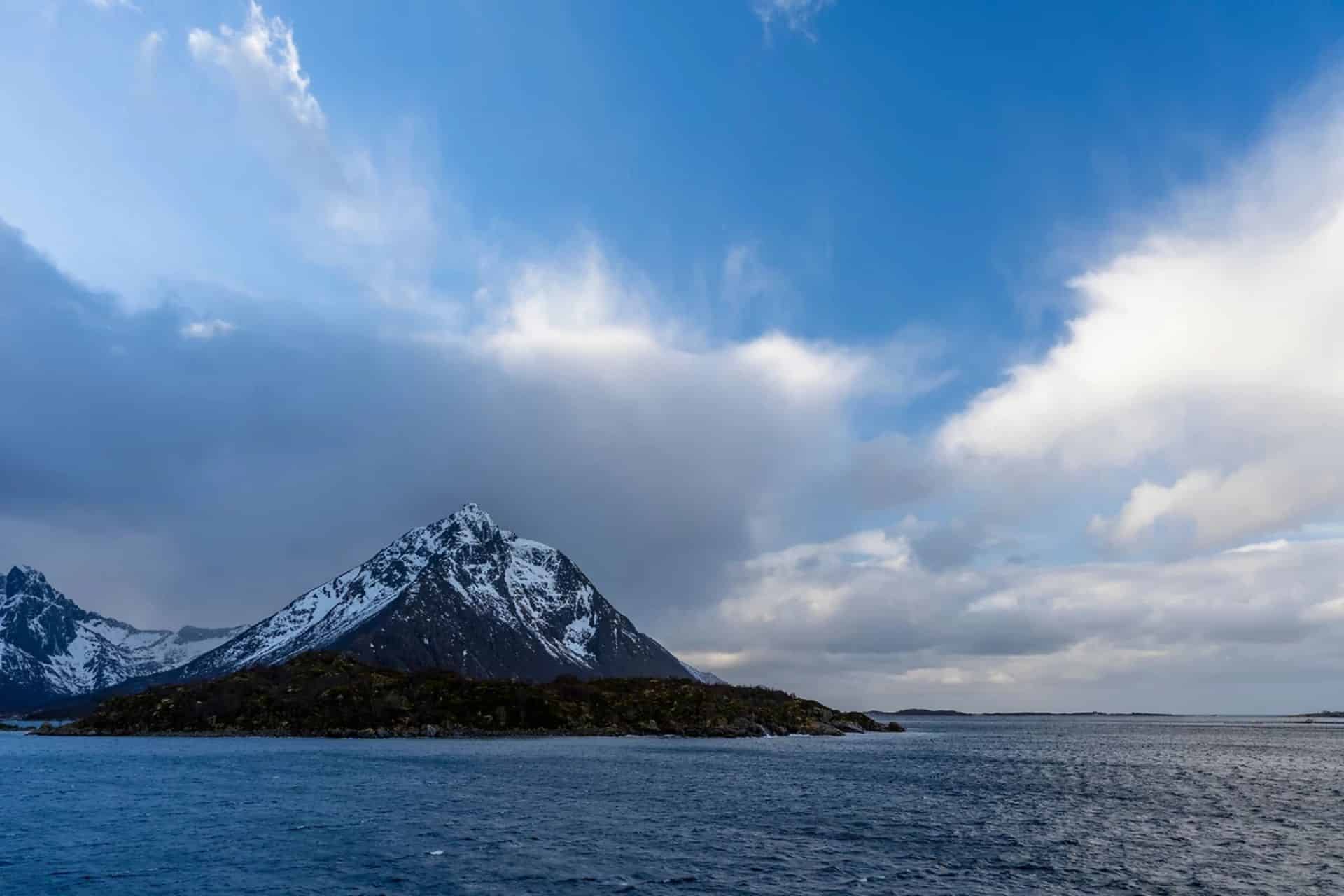 http://Montagne%20enneigée%20dominant%20un%20fjord%20avec%20mer%20calme%20et%20ciel%20nuageux