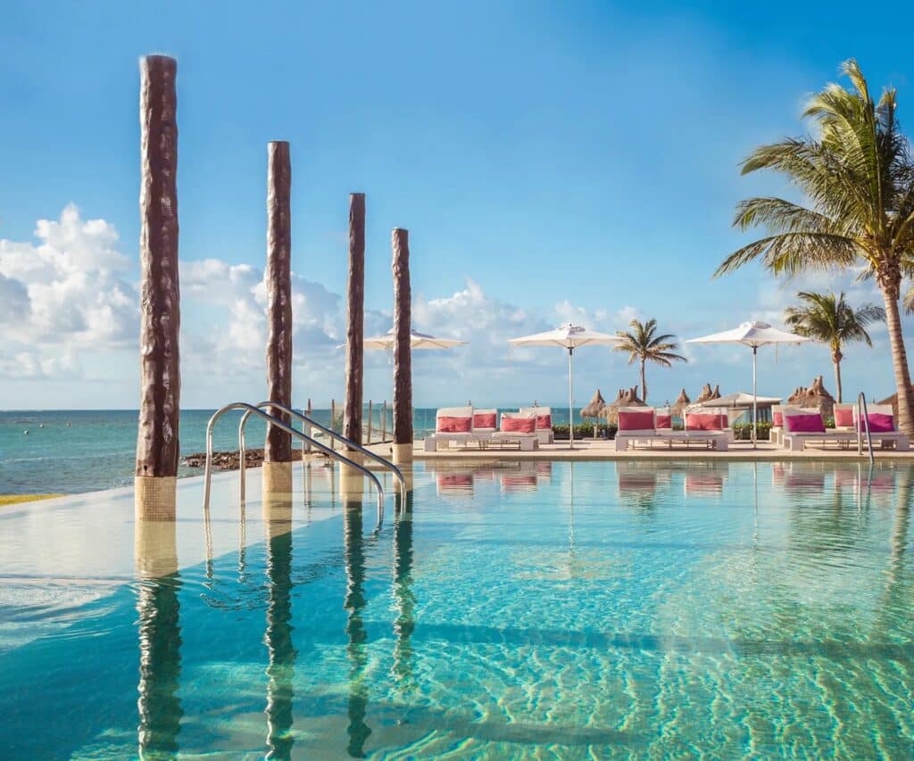 Piscine à débordement face à l’océan avec transats et palmiers