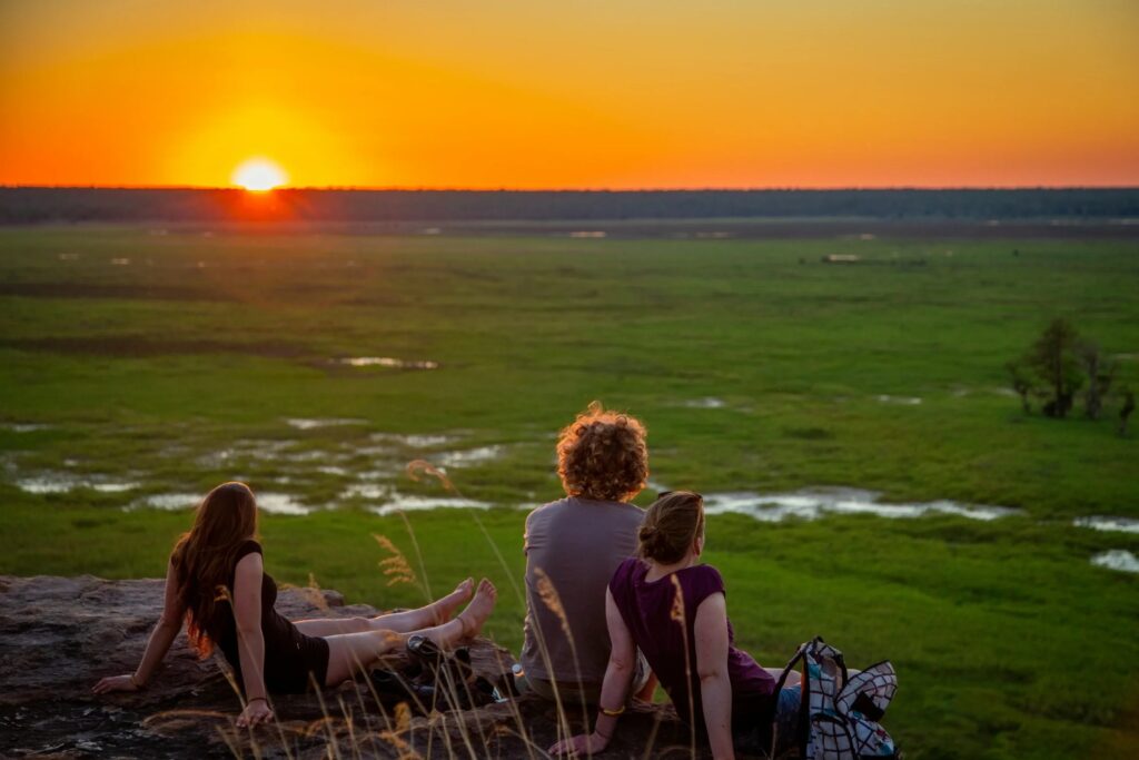 Trois voyageurs admirant un coucher de soleil sur un vaste paysage naturel