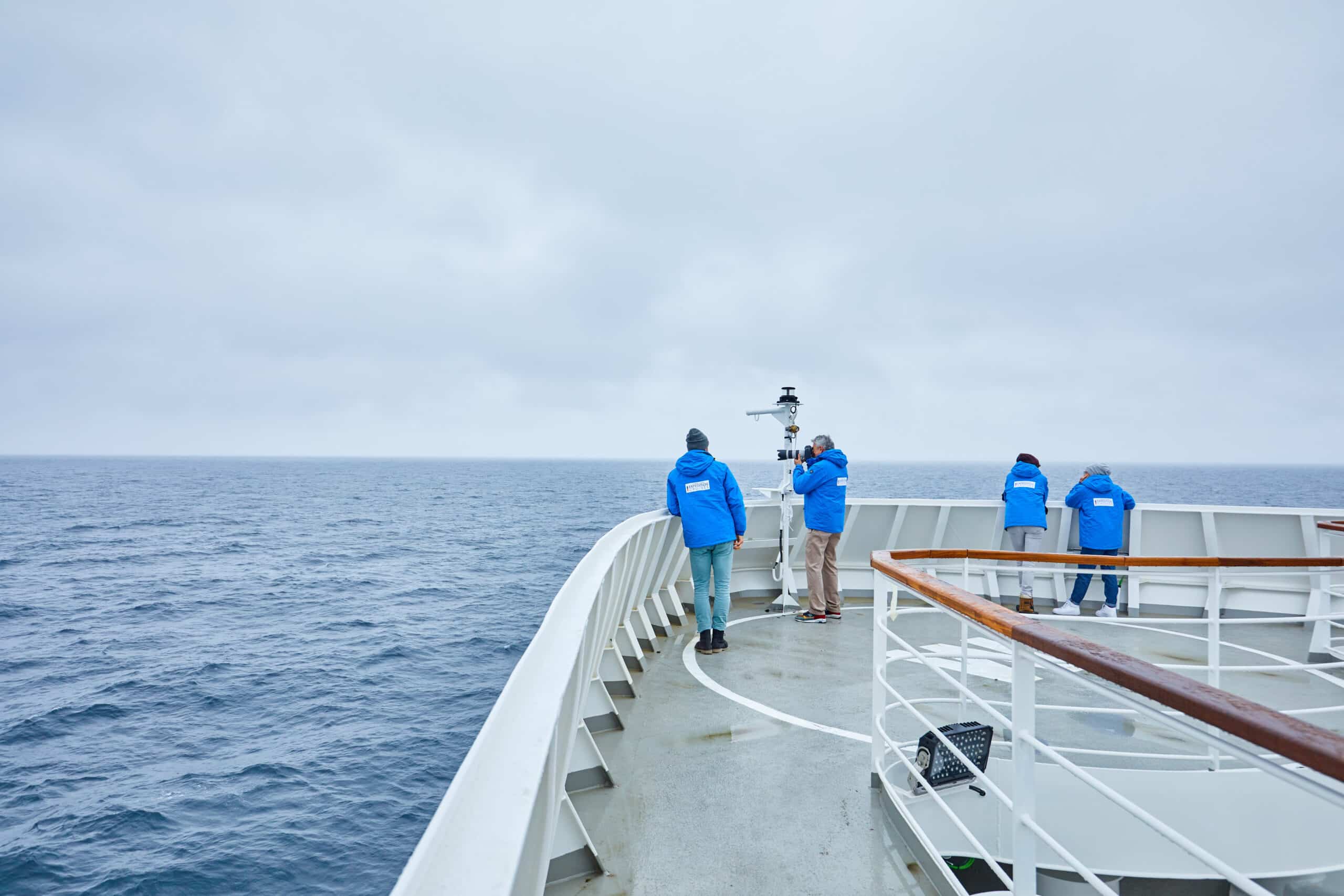 http://Passagers%20en%20veste%20bleue%20observant%20l’océan%20depuis%20le%20pont%20d’un%20bateau%20de%20croisière%20d’expédition