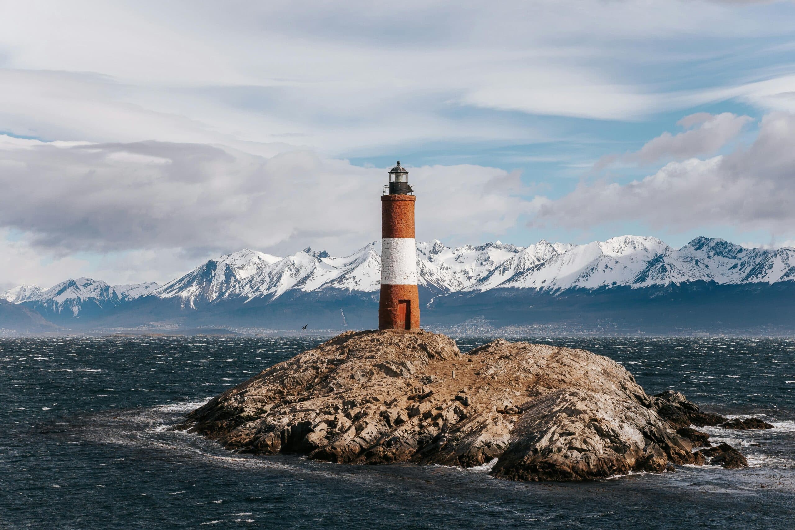 http://Phare%20rouge%20et%20blanc%20sur%20une%20île%20rocheuse%20avec%20montagnes%20enneigées%20en%20arrière-plan