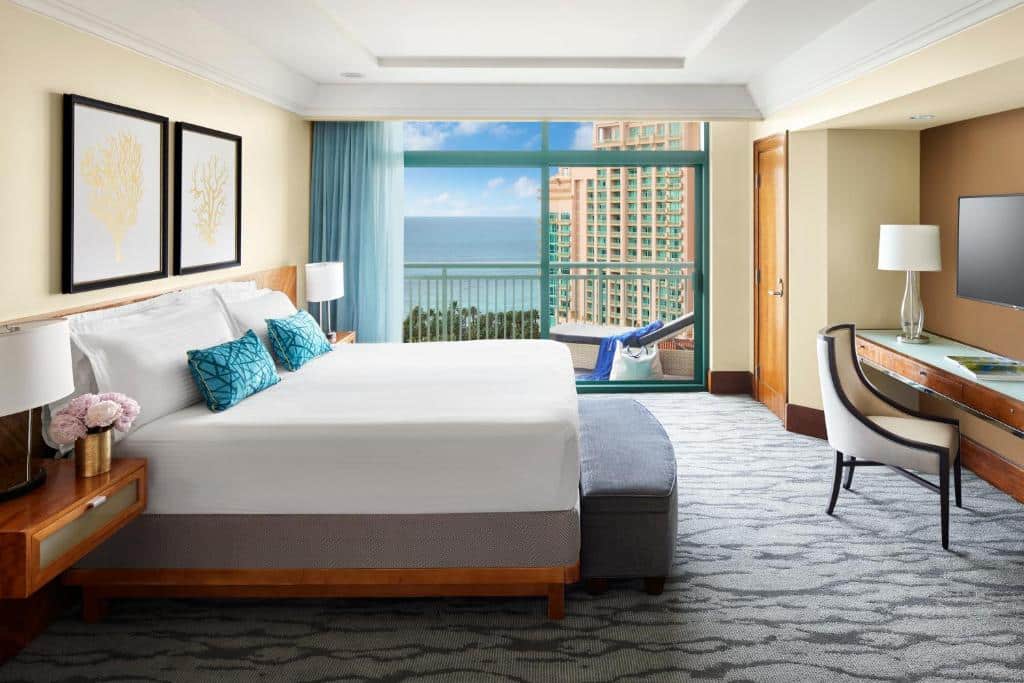 http://Chambre%20d'hôtel%20spacieuse%20avec%20balcon%20privé%20offrant%20une%20vue%20sur%20l'océan%20et%20un%20complexe%20balnéaire%20aux%20Bahamas.