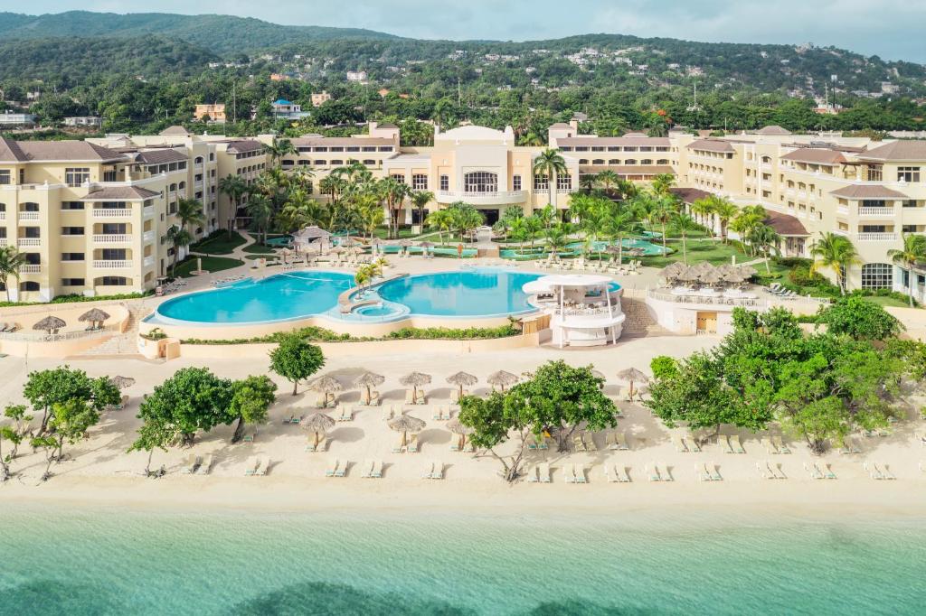 Vue aérienne d’un resort en bord de mer avec grande piscine, plage de sable blanc et eaux turquoise en Jamaïque.