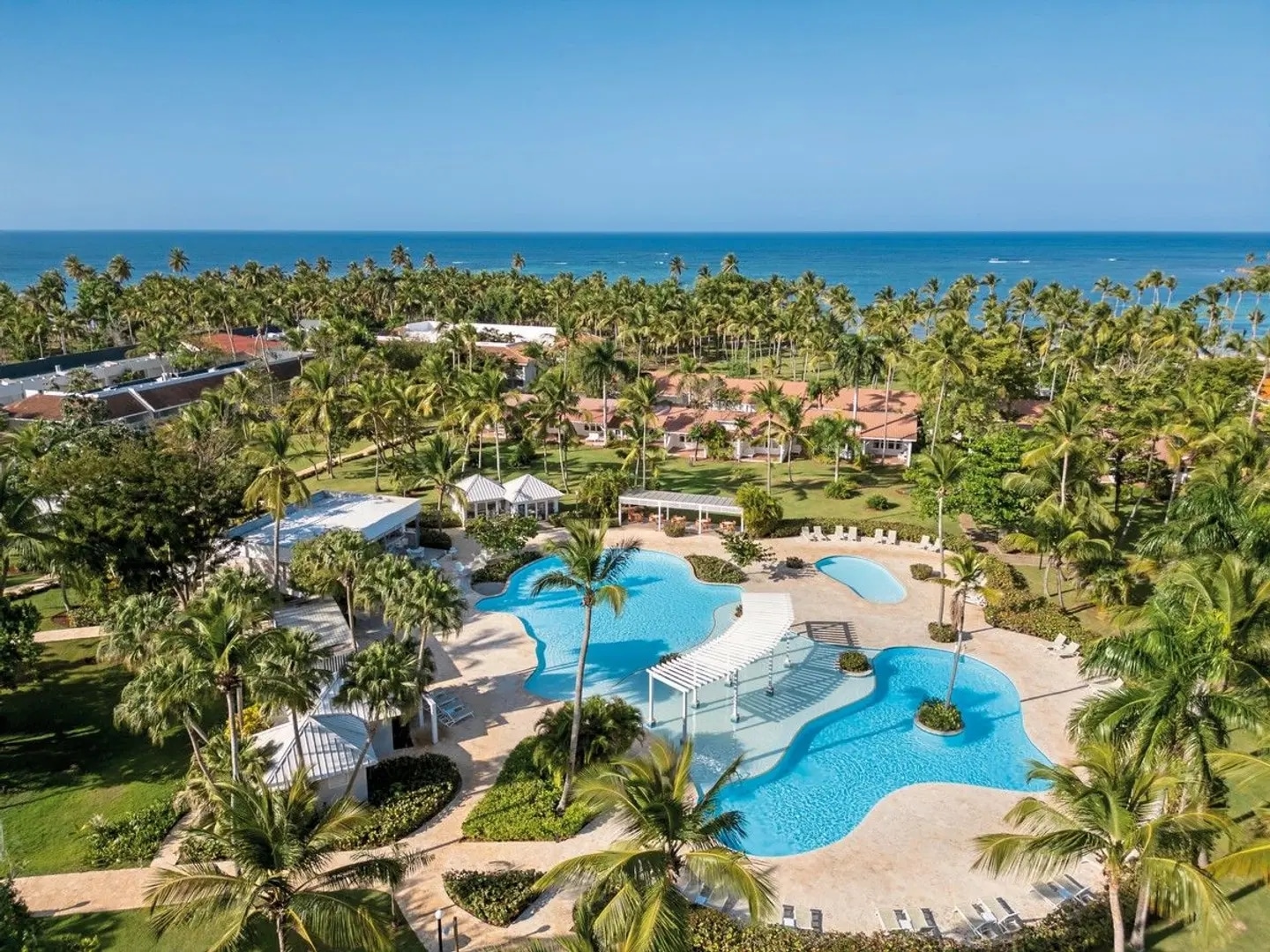 http://Grande%20piscine%20extérieure%20entourée%20de%20palmiers%20au%20sein%20d'un%20complexe%20hôtelier%20en%20République%20dominicaine.