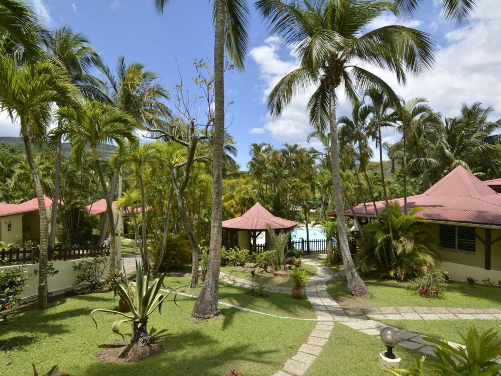 Allée bordée de palmiers et de végétation tropicale menant aux hébergements d'un resort aux Antilles.