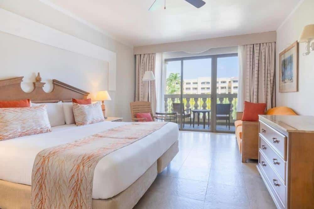 http://Chambre%20d’hôtel%20lumineuse%20avec%20grand%20lit%20double,%20coin%20salon%20et%20balcon%20privé%20donnant%20sur%20les%20jardins%20du%20complexe.