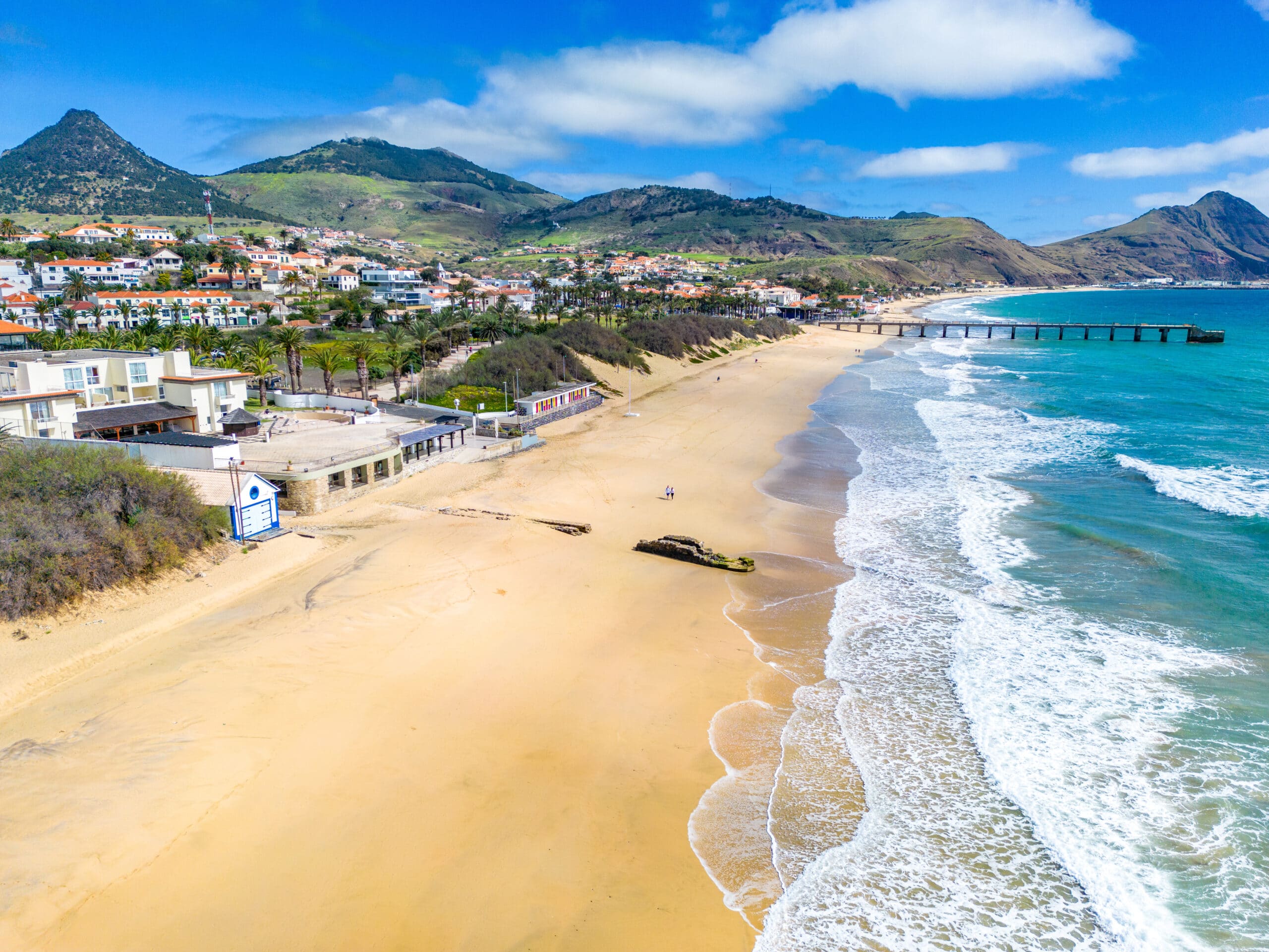 http://Vue%20aérienne%20de%20la%20plage%20de%20Vila%20Baleira%20à%20Porto%20Santo%20avec%20promenade,%20jetée,%20habitations%20et%20montagnes.