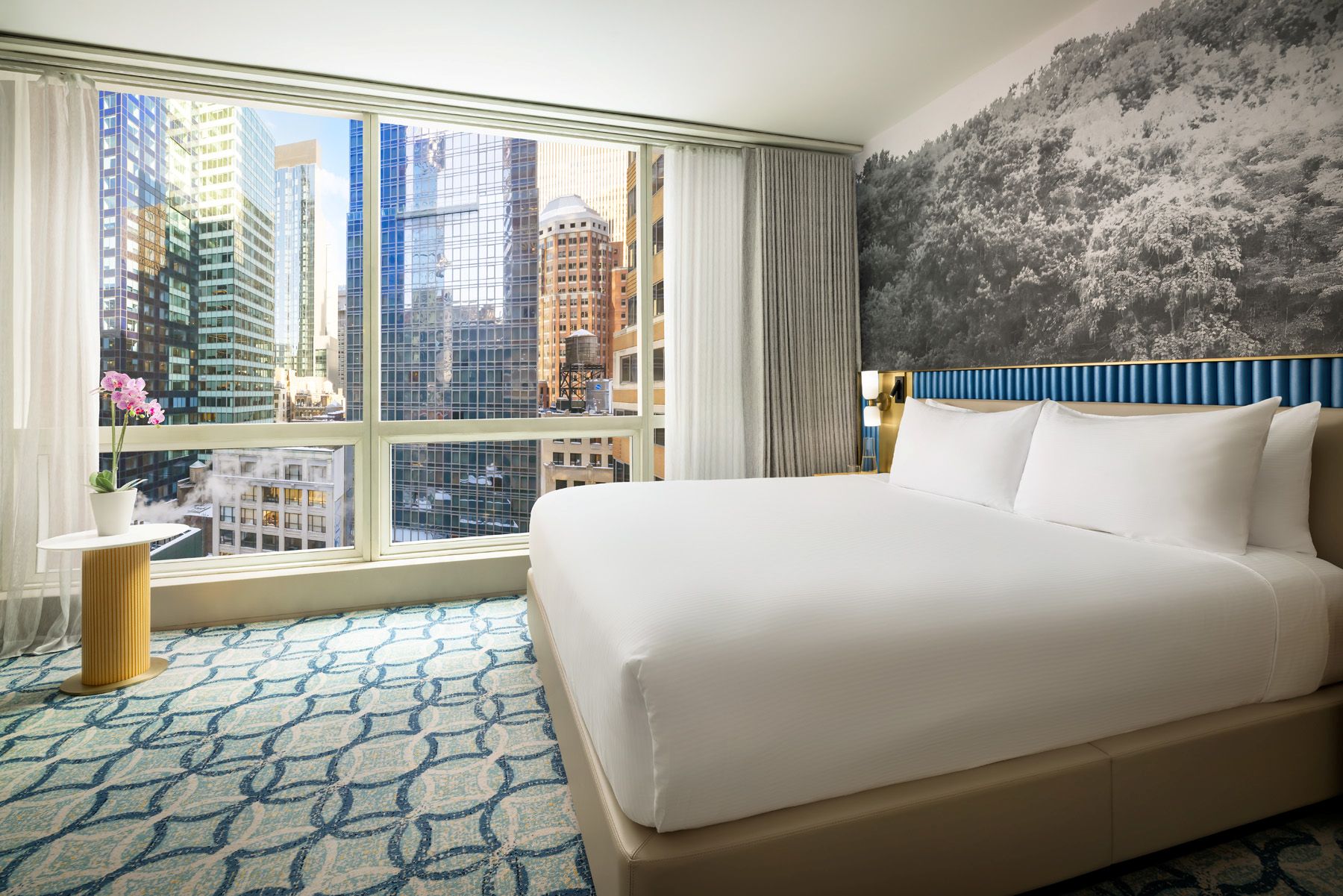 http://Chambre%20d’hôtel%20avec%20grand%20lit%20et%20baie%20vitrée%20donnant%20sur%20les%20gratte-ciel%20de%20Manhattan%20à%20New%20York.
