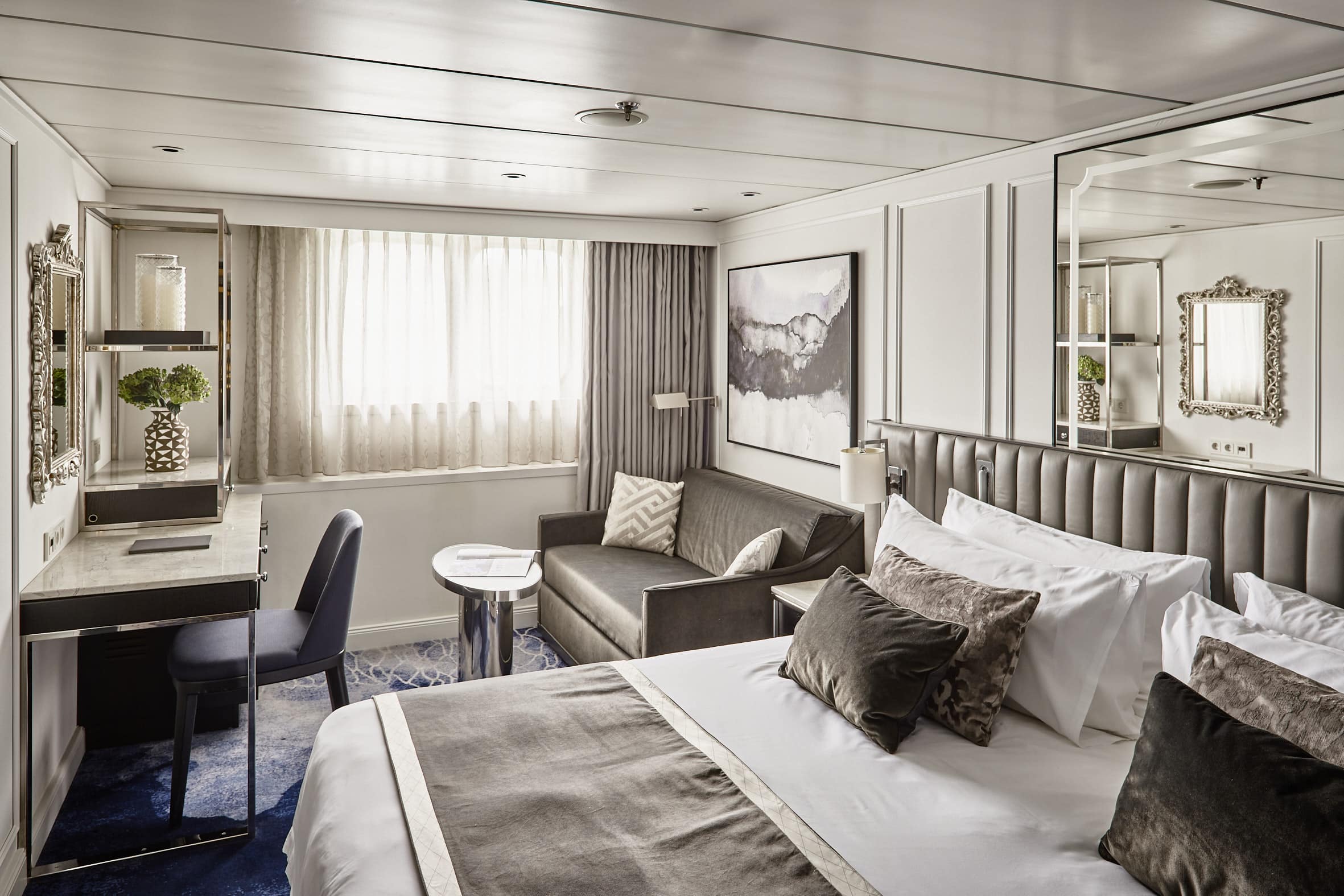 Cabine élégante de bateau de croisière fluviale avec lit double, canapé et espace bureau.