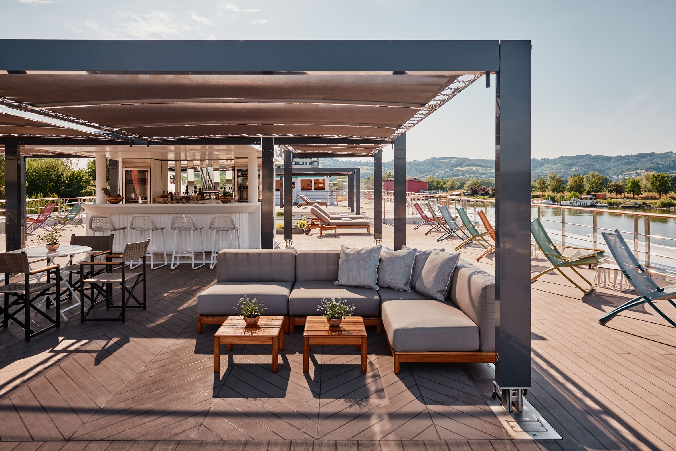 Pont extérieur d’un bateau de croisière fluviale avec bar, salon et transats face au paysage.