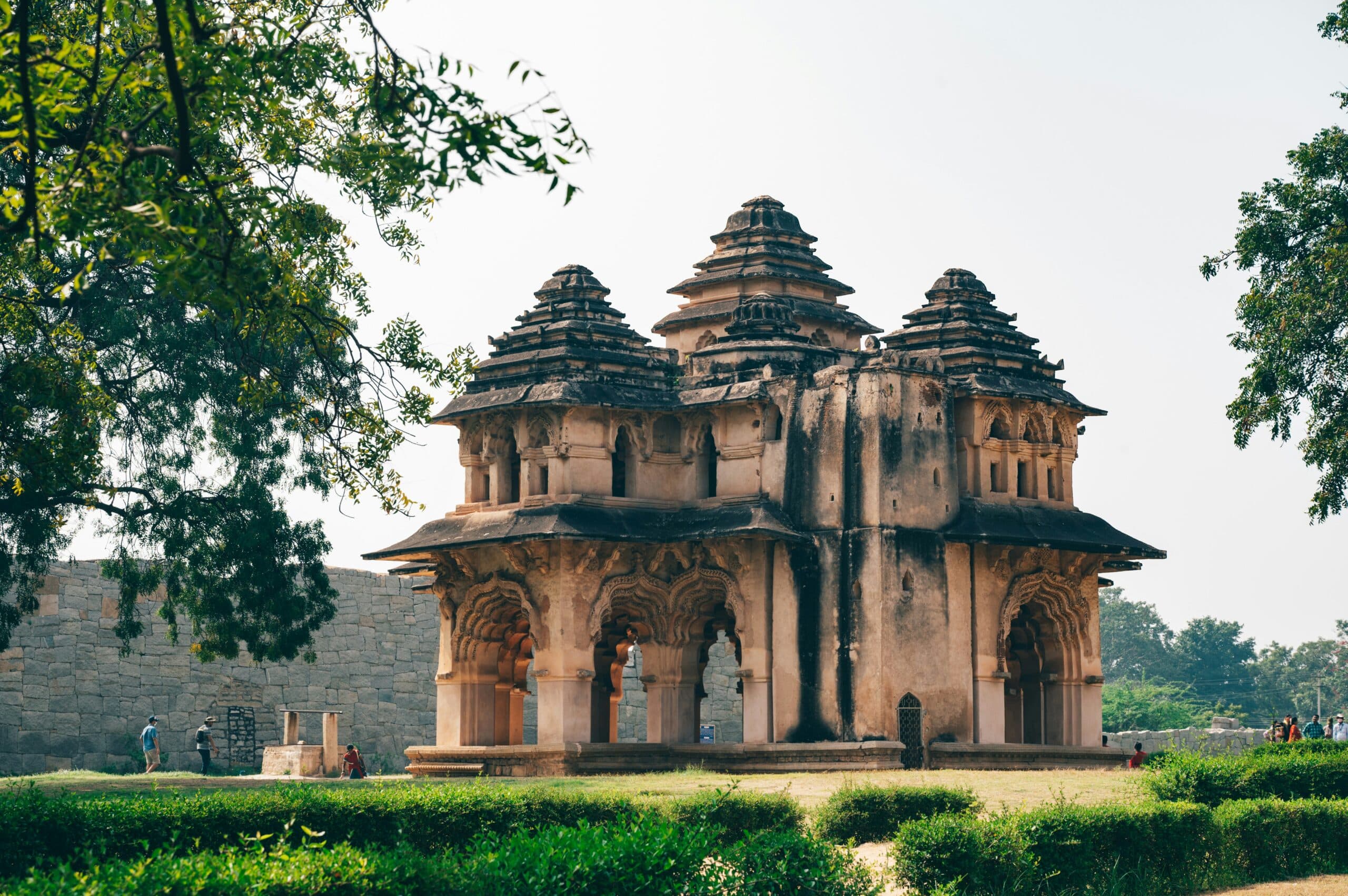 http://Lotus%20Mahal%20à%20Hampi,%20édifice%20historique%20aux%20arches%20sculptées%20et%20pavillons%20superposés%20entouré%20de%20jardins.