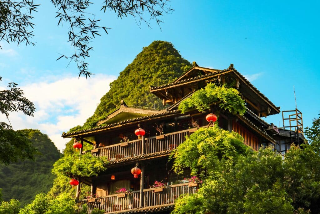 Maison traditionnelle chinoise en bois décorée de lanternes rouges au pied de montagnes verdoyantes.