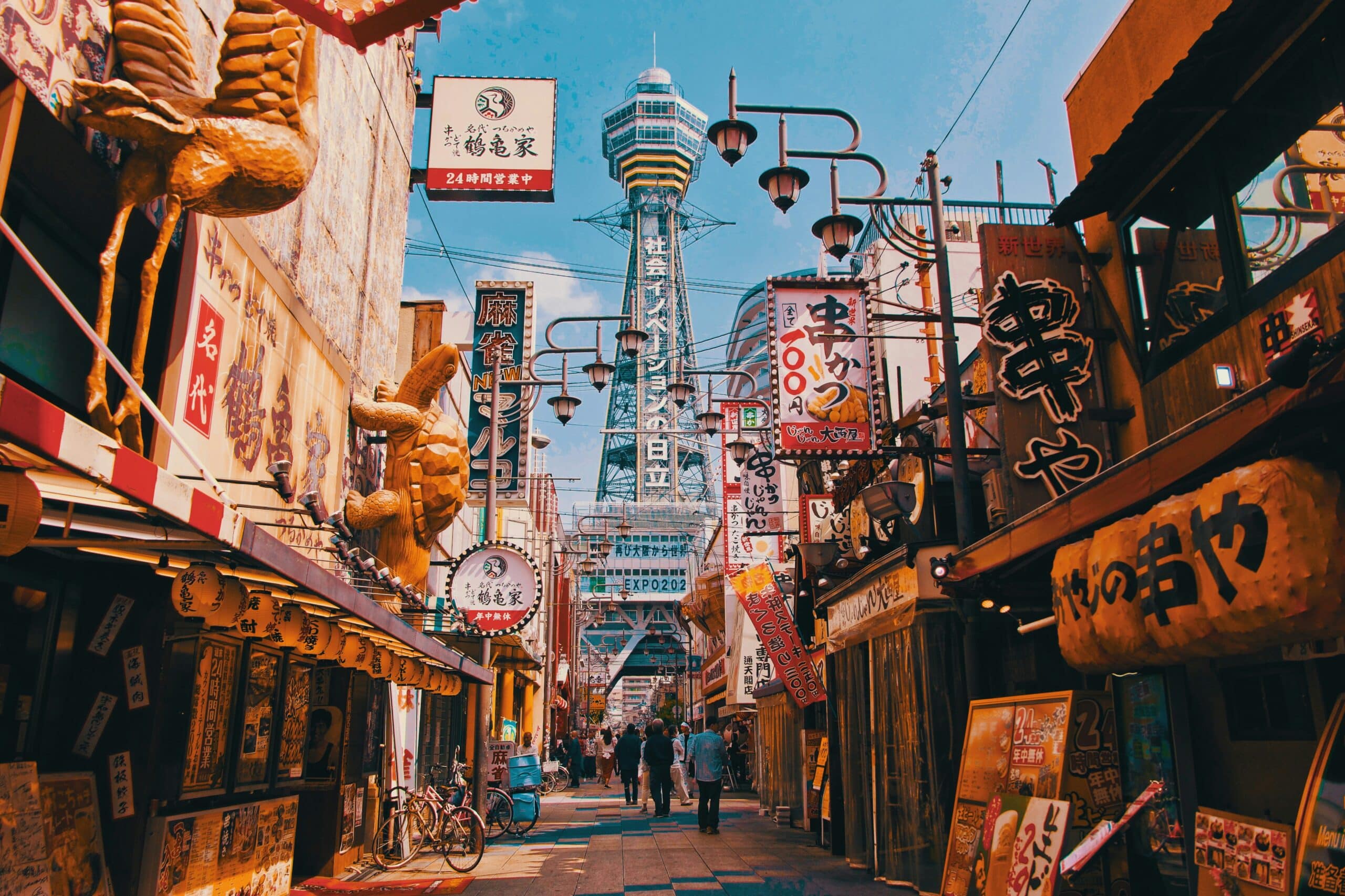 http://Rue%20animée%20du%20quartier%20Shinsekai%20à%20Osaka%20avec%20ses%20enseignes%20lumineuses,%20ses%20restaurants%20et%20la%20tour%20Tsutenkaku%20en%20arrière-plan.