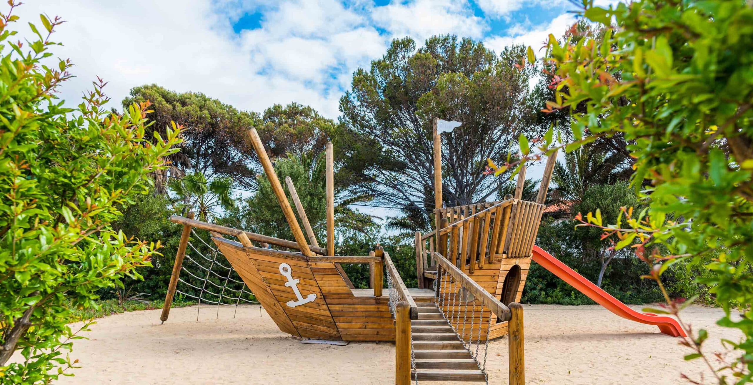 http://Aire%20de%20jeux%20extérieure%20pour%20enfants%20avec%20bateau%20en%20bois,%20toboggan%20et%20structures%20d’escalade%20dans%20les%20jardins%20de%20l’hôtel.