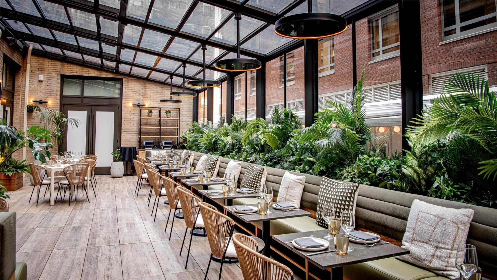 http://Restaurant%20lumineux%20sous%20une%20verrière%20avec%20tables%20dressées%20et%20végétation%20abondante%20à%20New%20York.