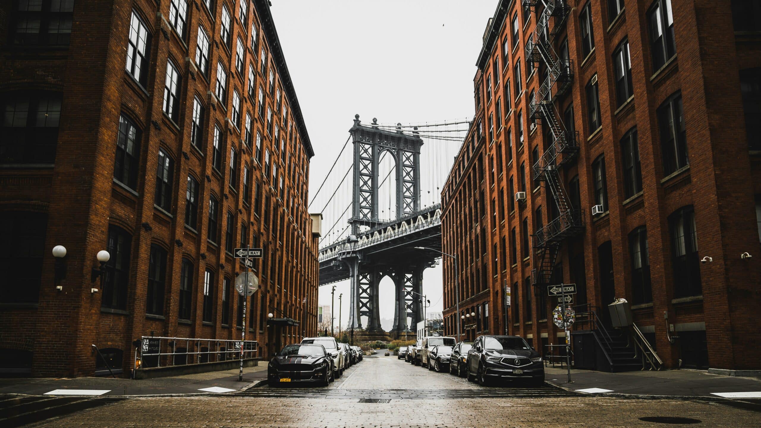 http://Manhattan%20Bridge%20vu%20depuis%20une%20rue%20bordée%20d’immeubles%20en%20briques%20dans%20le%20quartier%20de%20DUMBO%20à%20Brooklyn.