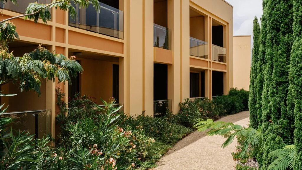 Façade d’un hôtel à Porto Santo avec balcons donnant sur un jardin arboré et une allée paysagère.