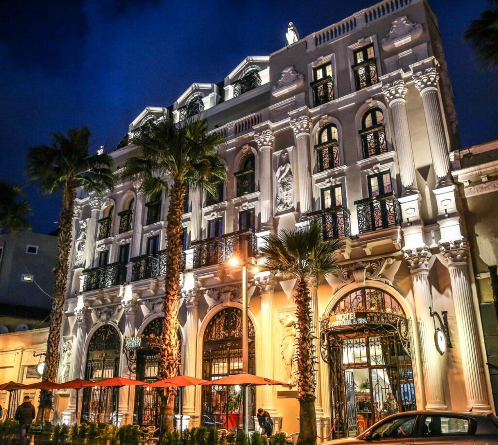 Façade illuminée de l’Epidamn Hotel Boutique & Spa à Durrës en Albanie, bordée de palmiers.