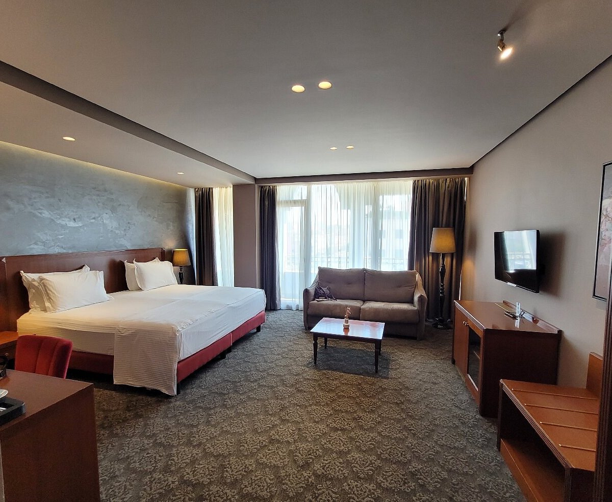 Chambre d’hôtel spacieuse en Albanie avec grand lit, canapé, télévision et baie vitrée.