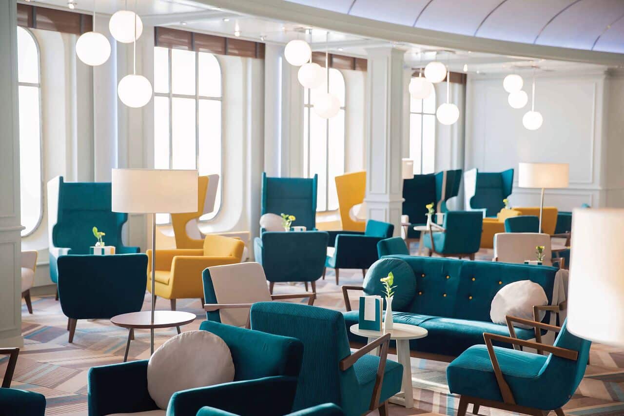 Salon lumineux d’un bateau de croisière avec fauteuils et canapés colorés aménagés près de grandes fenêtres