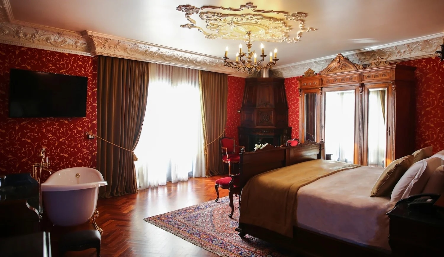 Chambre d’hôtel de luxe en Albanie avec grand lit, baignoire et décoration classique rouge et bois.