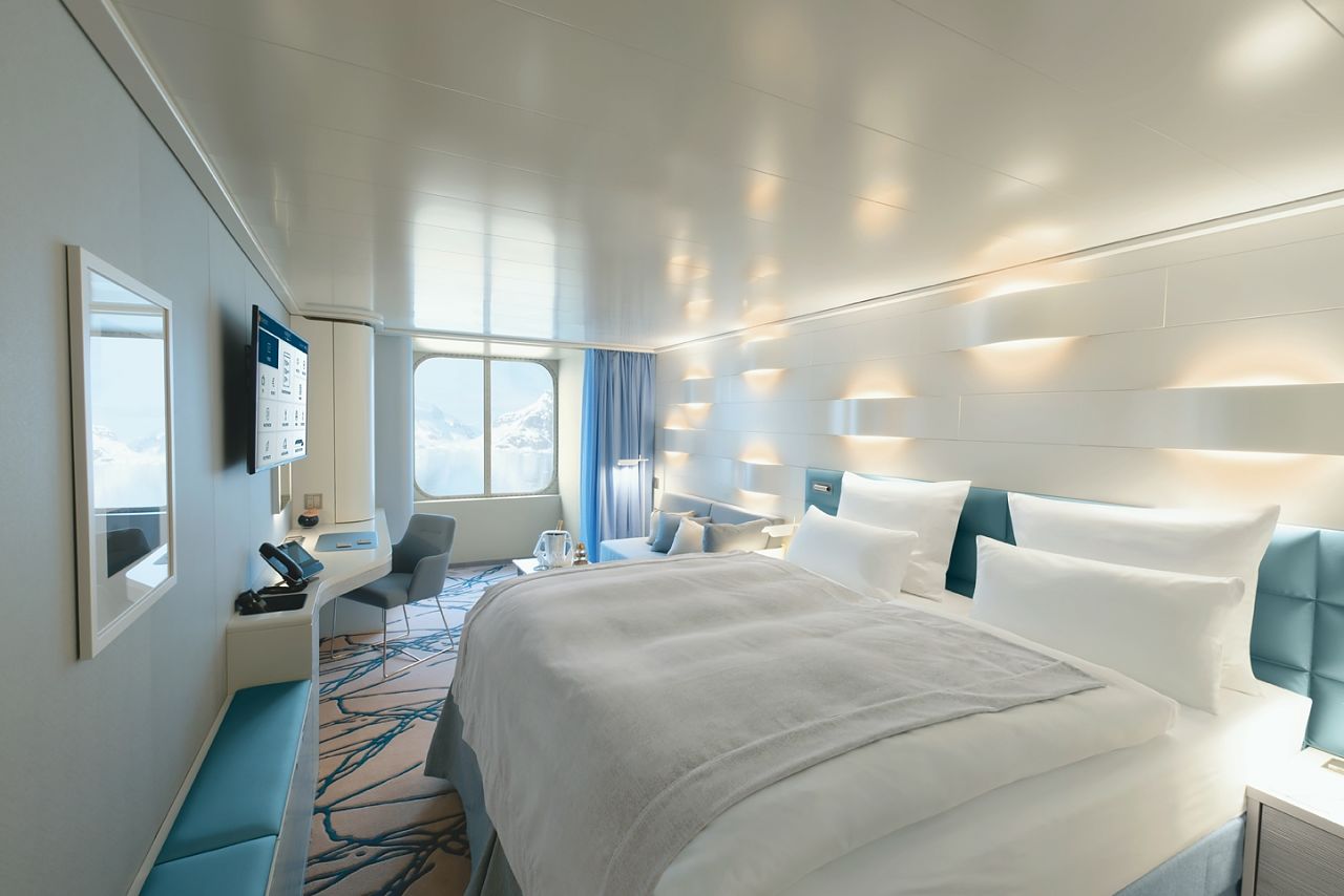 Cabine moderne de bateau de croisière avec grand lit et fenêtre panoramique donnant sur le paysage.