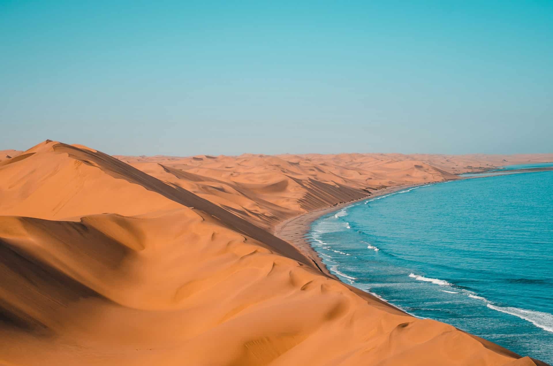 Les dunes géantes du désert du Namib plongeant dans les eaux de l’Atlantique à Sandwich Harbour, Namibie.