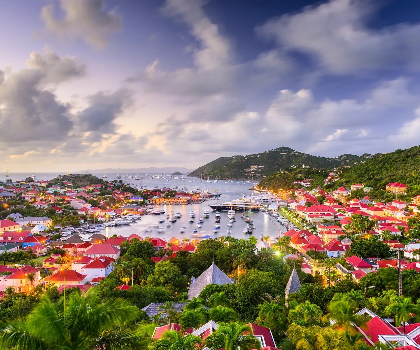Vue panoramique du port de Gustavia à Saint-Barthélemy au crépuscule, avec ses maisons aux toits rouges, ses yachts et ses collines verdoyantes.